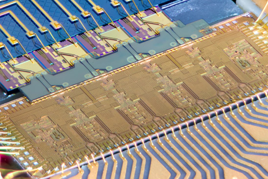 Eine Art Mikrochip mit blauen, goldenen Platinen und blaugefärbten Linien repräsentiert eine hybride photonische integrierte Schaltung.