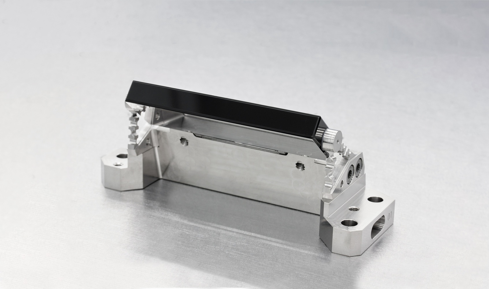 Abb. 1: Einer der beiden Umlenkspiegel, eingeklebt in eine Halterung aus Titan. Rechts und links sind v-förmig die Festkörpergelenke zu erkennen. Einer der beiden Umlenkspiegel, eingeklebt in eine Halterung aus Titan. Rechts und links sind v-förmig die Festkörpergelenke zu erkennen.