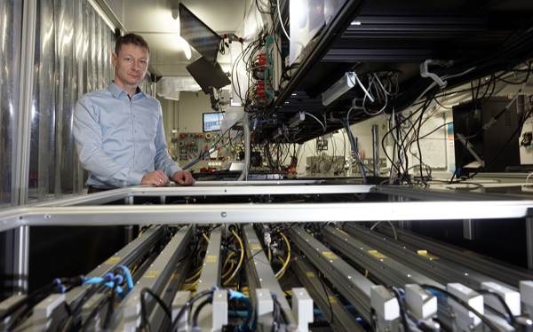 Prof. Dr. Jens Limpert im Labor neben dem technischen Aufbau des Hochleistungs&amp;shy;faserlaser&amp;shy;systems zur Erzeugung kohärenter Laserpulse.