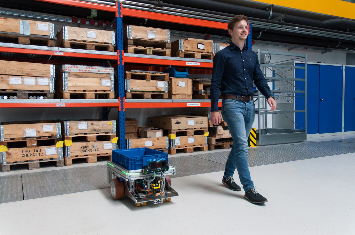 The FOLLOWme robot next to warehouse shelves.