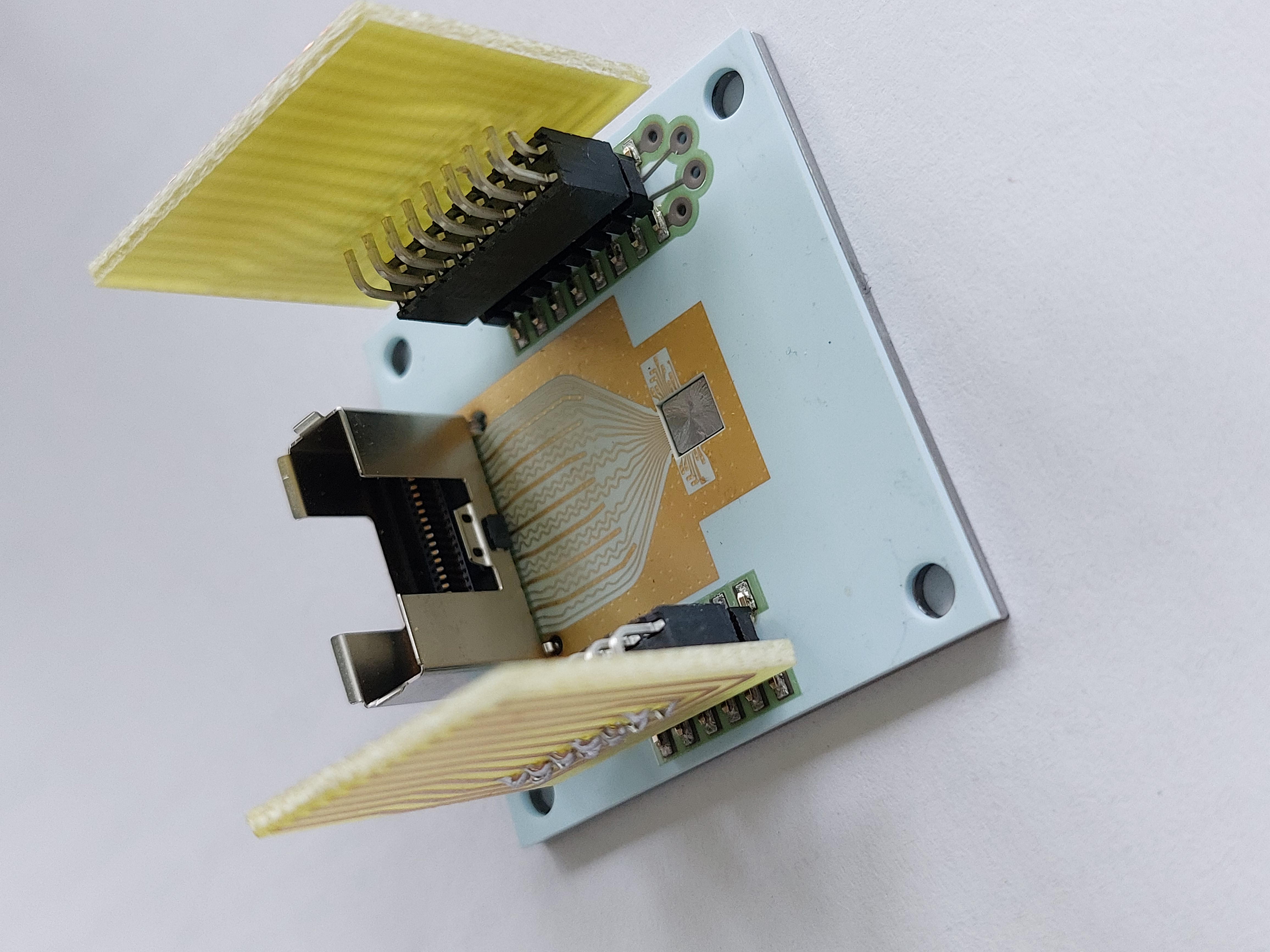 A ceramic printed circuit board (PCB) is bonded to a molybdenum heatsink. The PCB carries the VCSEL and driver chip (center). The wings are plugs for thermal management components. A ceramic printed circuit board (PCB) is bonded to a molybdenum heatsink. The PCB carries the VCSEL and driver chip (center). The wings are plugs for thermal management components.