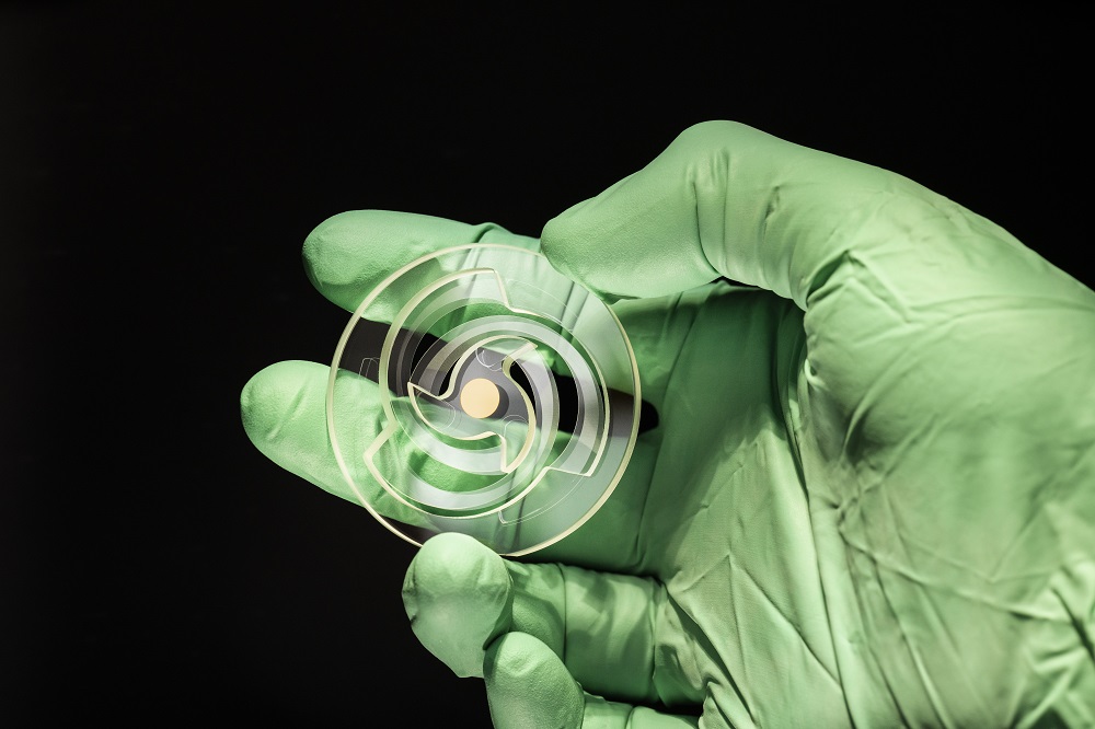 Monolithic glass resonator is presented by a hand wearing a green rubber glove of the camera.